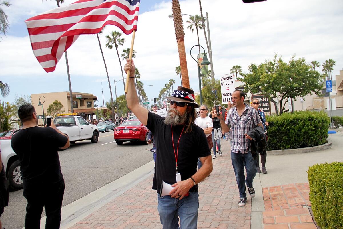 A man carries an American flag on a sidewalk.