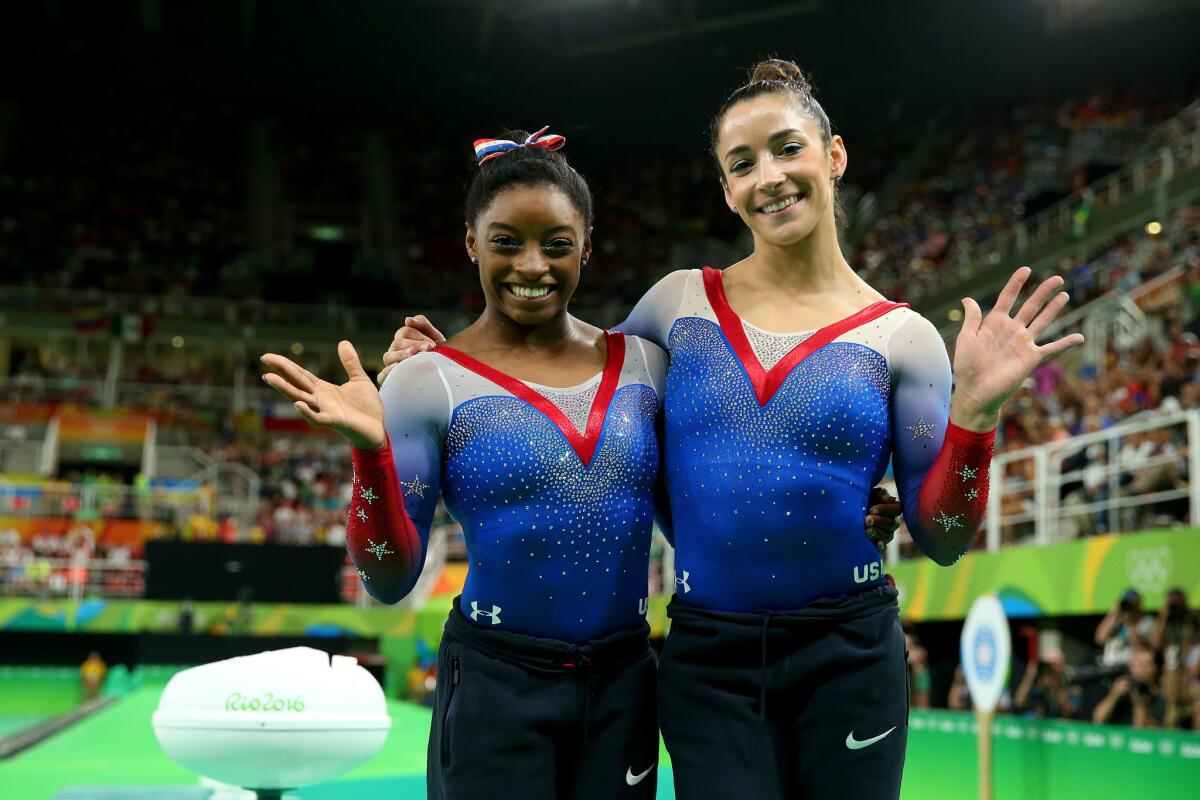 Simone Biles and Aly Raisman wave after finishing 1-2 in the floor exercise.