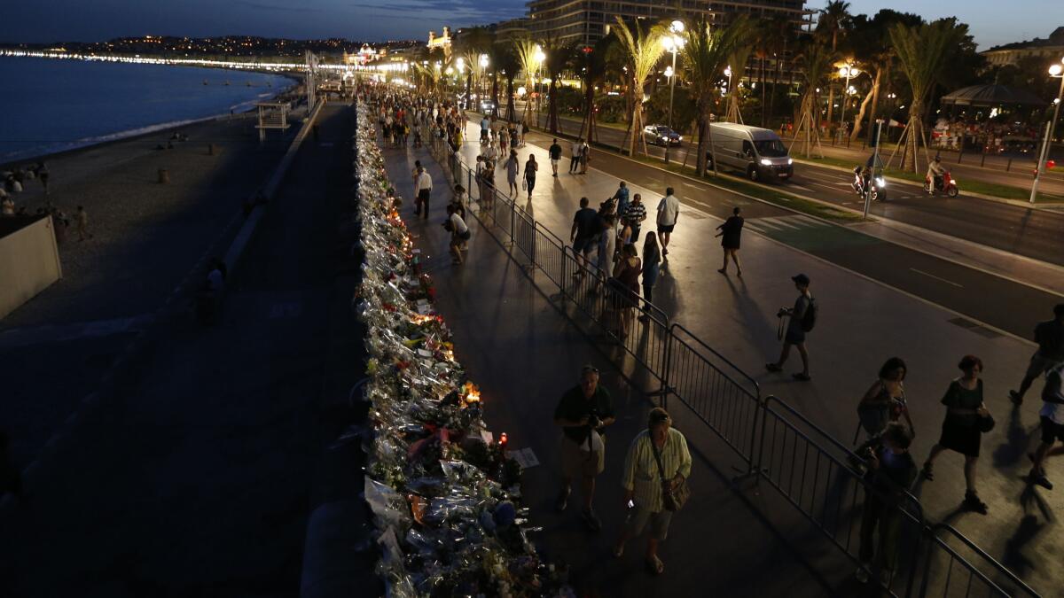 People walk on the Promenade des Anglais in Nice, France, on July 20, 2016, next to floral tributes, notes and candles placed in the road for victims of the deadly Bastille Day attack.