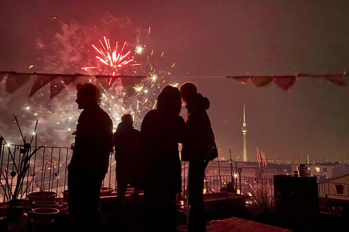 A small group of people silhouetted against a sky glowing with fireworks