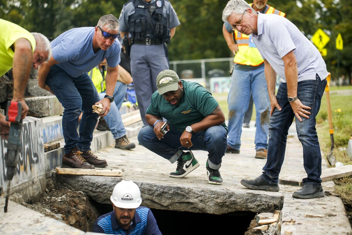 Devon Henry, owner of the construction company that removed the Confederate Gen. Robert E. Lee statue, center, looks on as crews work on retrieving a 134-year-old time capsule at Monument Avenue, Thursday, Sept. 9, 2021, in Richmond, Va. The time capsule will be replaced with a new one. (Shaban Athuman/Richmond Times-Dispatch via AP)