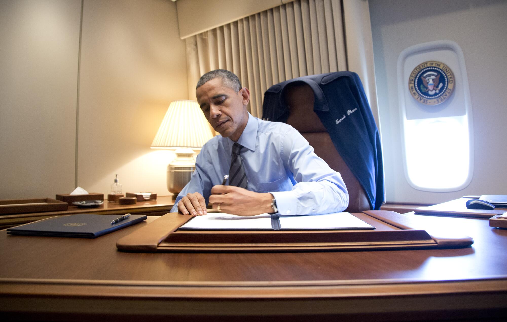 President Obama signing documents at a desk on Air Force One