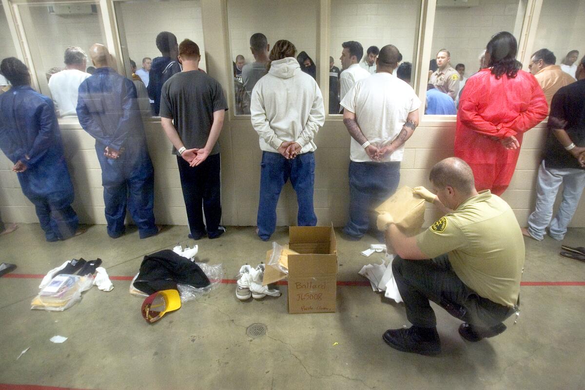 Men stand facing a wall while a deputy goes through their belongings.