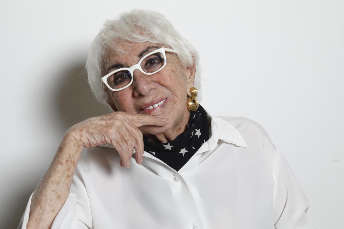 A woman with white hair and white glasses smiles at the camera.