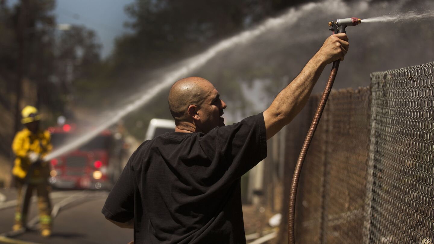 Area resident Pascual Gutierrez uses a garden hose as he works alongside firefighters battling a blaze that threatened structures along the 2 Freeway where it meets the 5 Freeway.