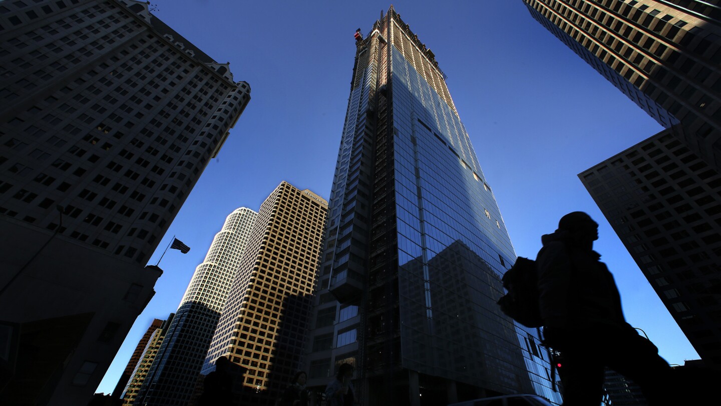 A pedestrian walks past the Wilshire Grand hotel, center, currently under construction at Wilshire Boulevard and Figueroa Street in downtown Los Angeles. When finished, the Wilshire Grand will rise 1,100 feet high and become the tallest building west of the Mississippi.