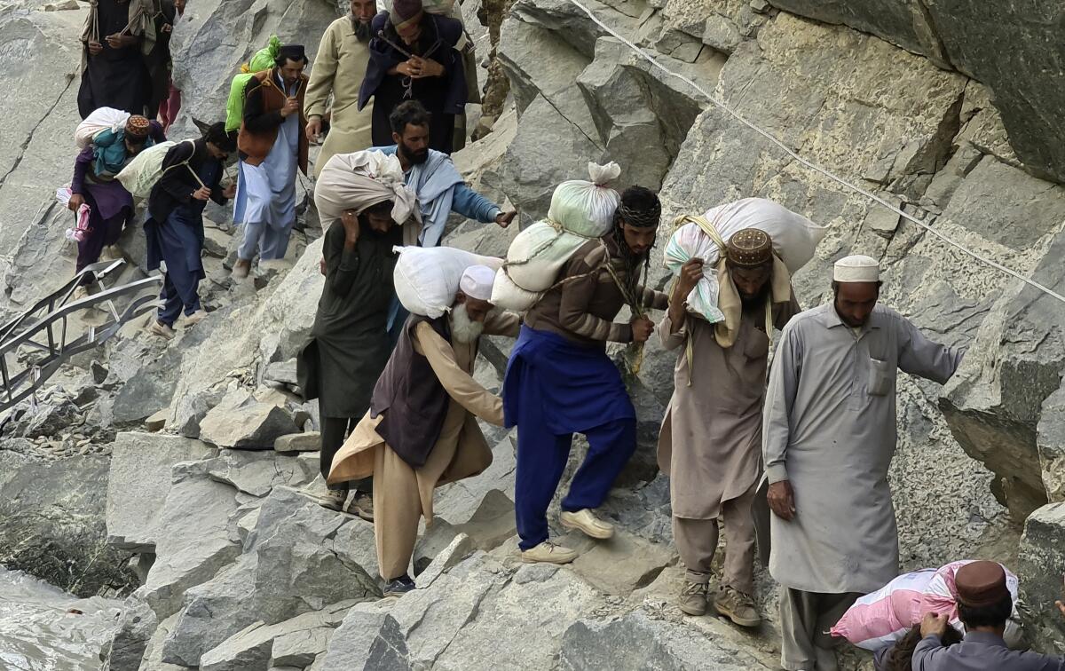 People in Pakistan cross a road destroyed by floodwaters