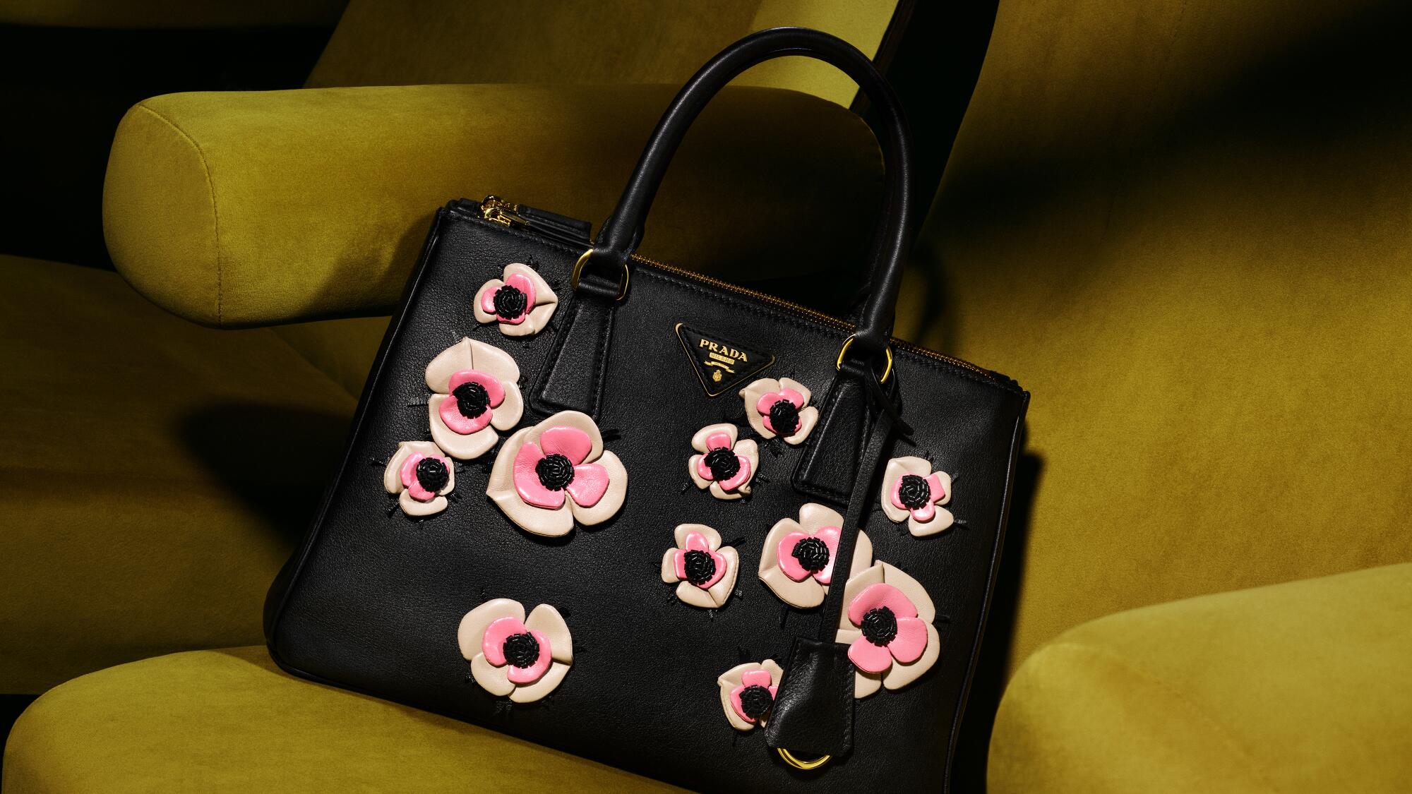 A black purse with pink appliqued flowers sits on a mustard-yellow chair