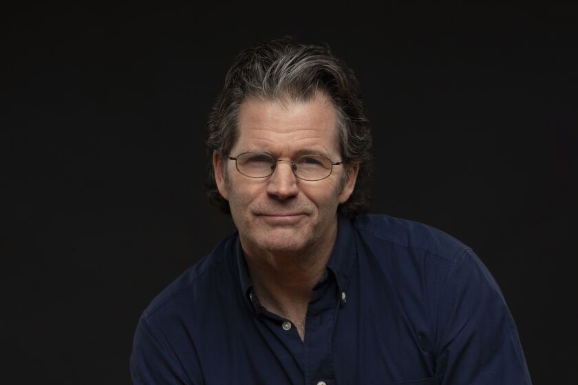 A man with glasses and a blue button-down shirt crouching slightly.
