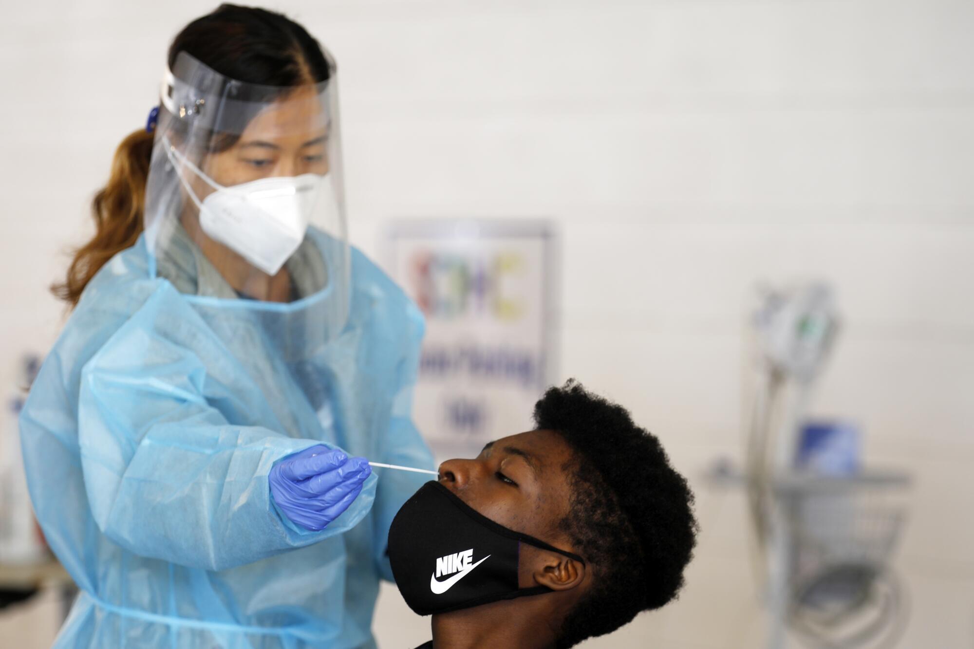 Dr. Grace Neuman, left, uses a Coronavirus nasal swab to test Kwesi Nelson 17, at Central Family Health Center on Tuesday