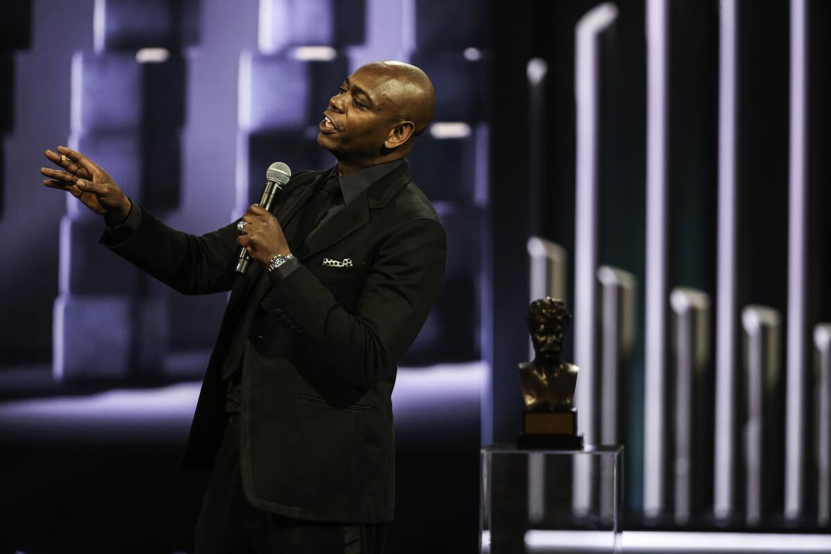 Dave Chappelle in a dark suit with a microphone 