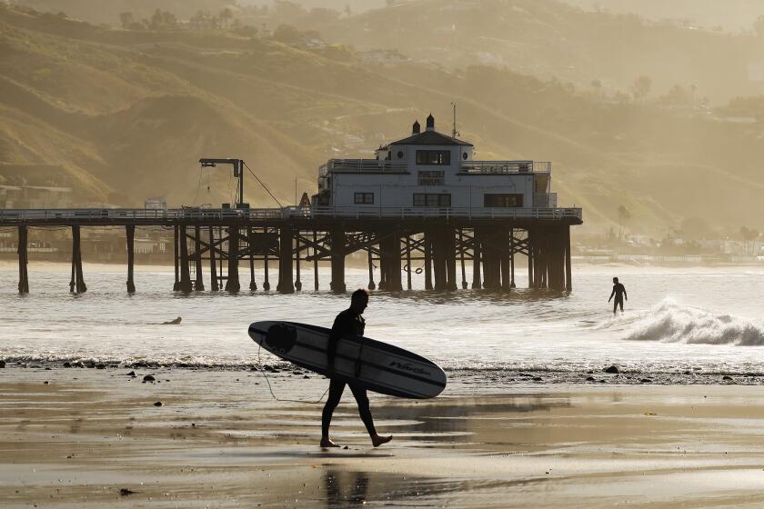 MALIBU, CA - MAY 13: Surfers take advantage of the low tide swell at Malibu Surfrider Beach next to the Malibu Pier Wednesday morning as Los Angeles County Beaches reopened for active use only. The beaches have been closed for two months due to the coronavirus Covid-19 pandemic and remained off limits even as the coastline reopened for active use in Orange County. Beachgoers will have to wear masks and maintain a six-foot buffer between themselves and others under continued social distancing requirements. Parking lots, piers and boardwalks will remain closed. Malibu Pier on Wednesday, May 13, 2020 in Malibu, CA. (Al Seib / Los Angeles Times)