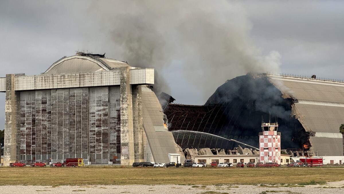 Smoke rises from the collapsed center of a blimp hangar in Tustin as fire crews shoot water onto it.