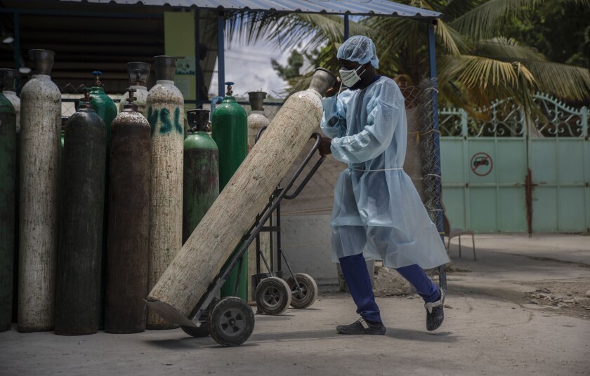 A hospital emplyee wearing protective gear as a precaution against the spread of the new coronavirus, transports oxygen tanks, in Port-au-Prince, Haiti, Saturday, June 5, 2021. Haiti defied predictions and perplexed health officials by avoiding a COVID-19 crisis for more than a year, but the country of more than 11 million people that has not received a single vaccine is now battling a spike in cases and deaths. (AP Photo/Joseph Odelyn)