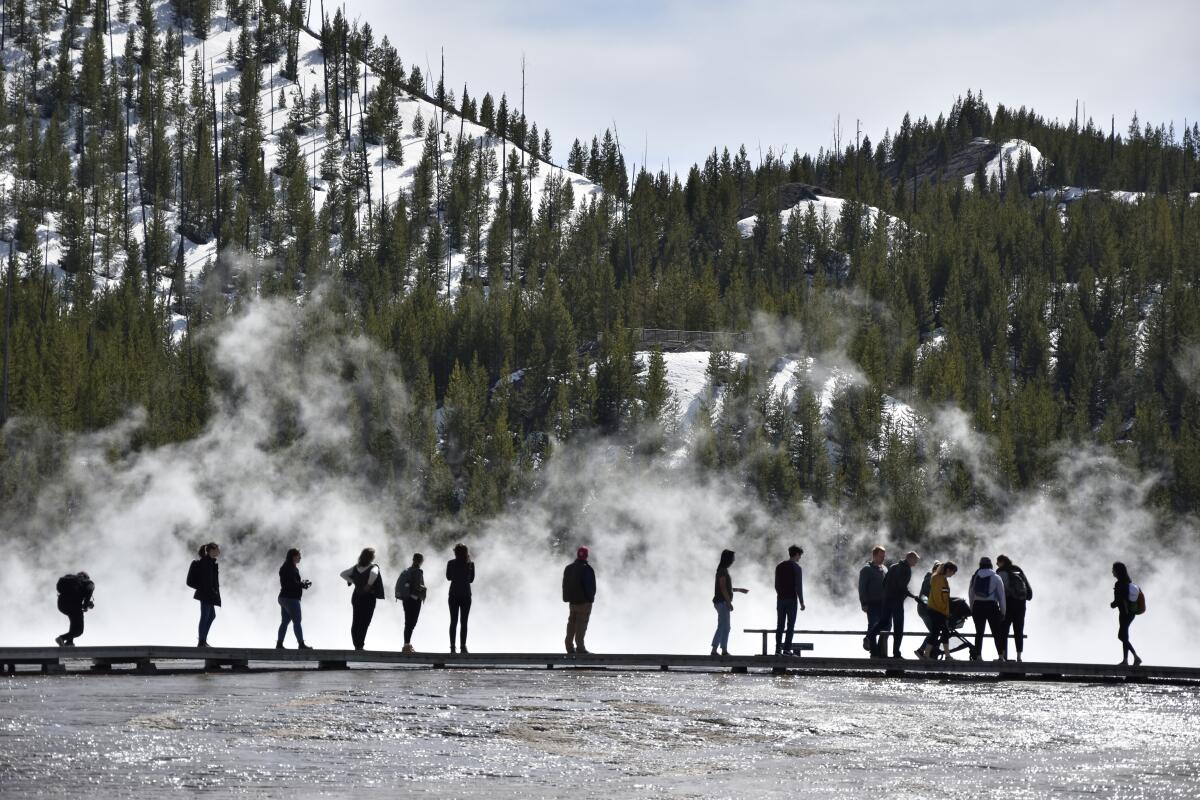 Tourists are silhouetted against rising mist and snowy slopes.