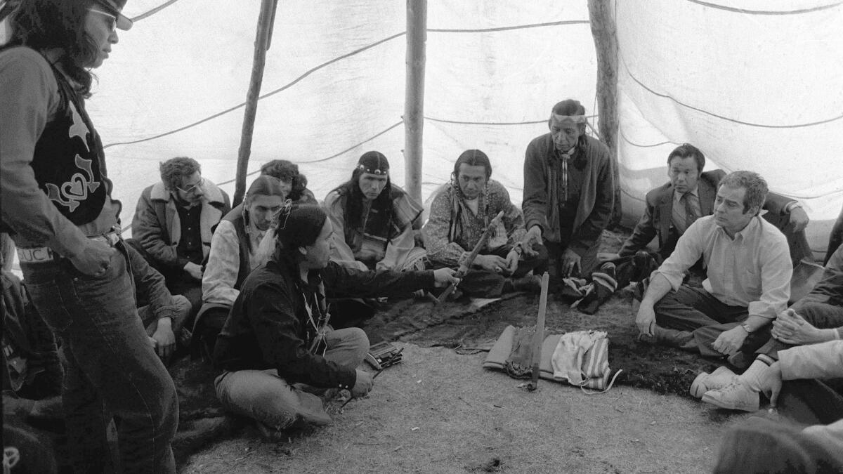 A member of the American Indian Movement (AIM), left, offers a peace pipe to Kent Frizzell, right, assistant U.S. attorney general, in a tepee at Wounded Knee, S.D., during a ceremony April 5, 1973, ending the bloody standoff between AIM and federal authorities.