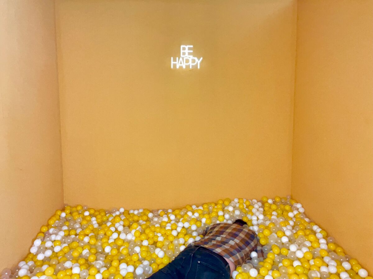 A man laying face down in a room full of plastic balls with a sign above that says be happy