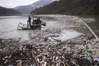 A small boat is shown amid piles of floating plastics near a shore.