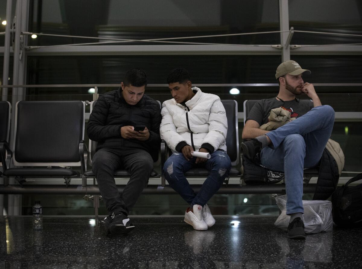 Three people sitting in a row of chairs at an airport