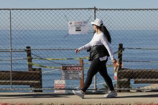 ENCINITAS, CA - JANUARY 12, 2024: A woman walks by signs and fencing that blocks the entrance to the Beacons Beach trail, which has been damaged from a landslide, in Encinitas on Friday, January 12, 2024.