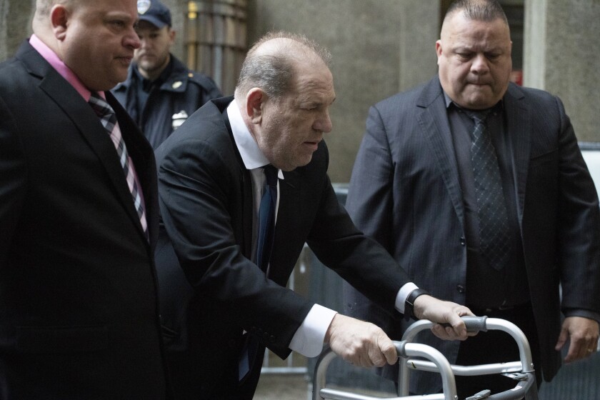 Harvey Weinstein uses a walker as two people accompany him outside a building