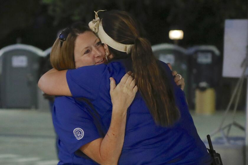 Festival volunteer Denise Buessing, left, embraces fellow volunteer Marsha Struzik on Sunday at a reunification center in a parking lot at Gavilan College in Gilroy.