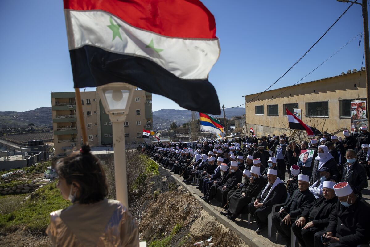 FILE - In this Feb. 14, 2021 file photo, Druse supporters of Syrian President Bashar Assad wave Syrian flags during a rally close to the Syrian border demanding the return of the Golan Heights, captured by Israel in 1967, in Majdal Shams, Golan Heights. The death of Midhat Saleh, a former Syrian Druse lawmaker, allegedly by Israeli sniper fire on Saturday, Oct. 16, 202, could mark a new phase in Israel’s war against Iranian entrenchment in neighboring Syria. Saleh was born in Majdal Shams, in the Israeli-controlled side of the Golan, and was jailed several times by Israel, most recently for 12 years until 1997. He later moved to Syria. (AP Photo/Oded Balilty, File)