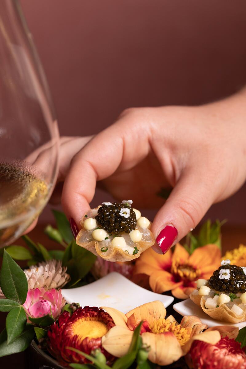 A hand places a shima aji tart with yuzu kosho and caviar among flowers and greens.