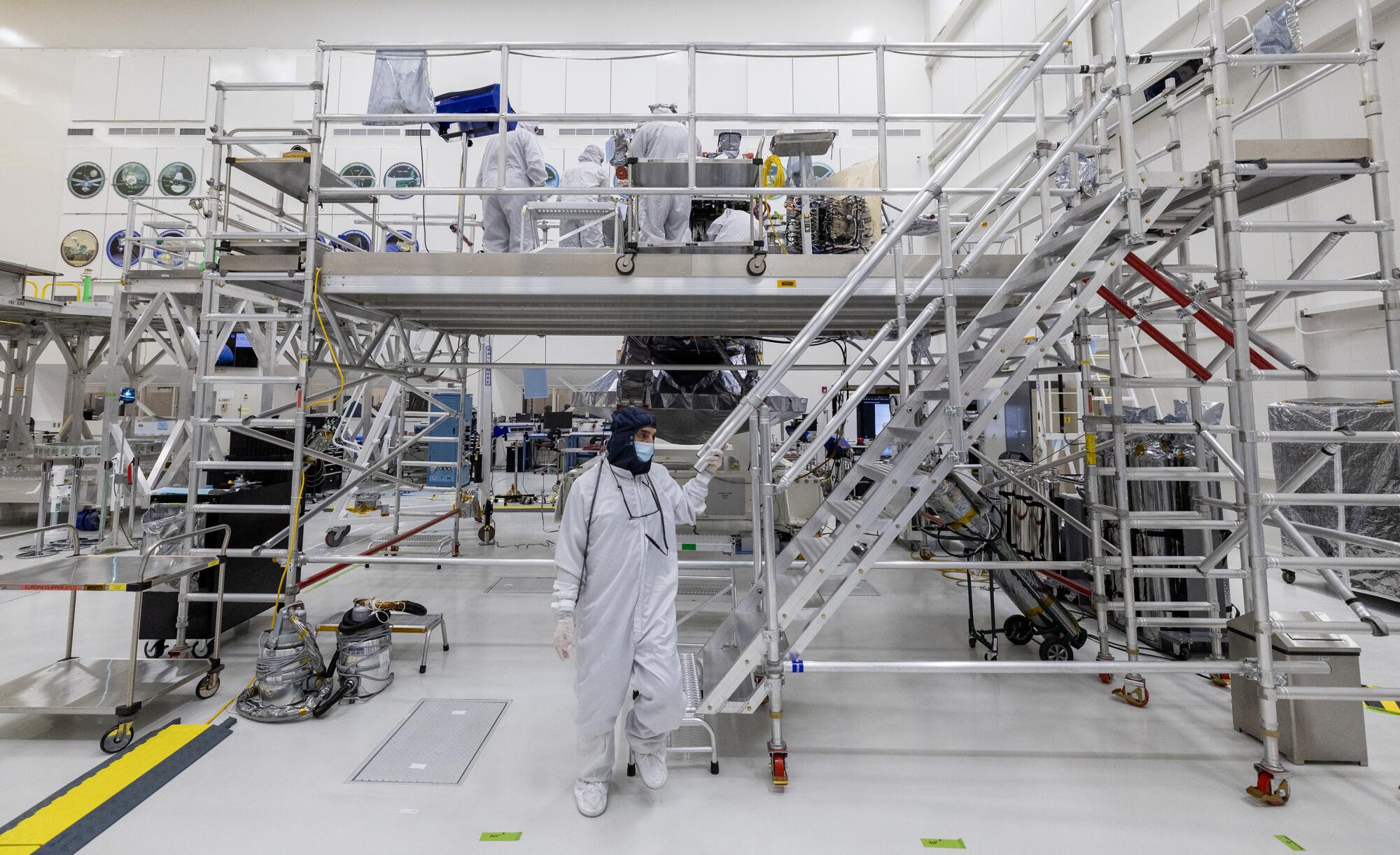 Engineers and technicians work on the Europa Clipper spacecraft, which is surrounded by scaffolding.