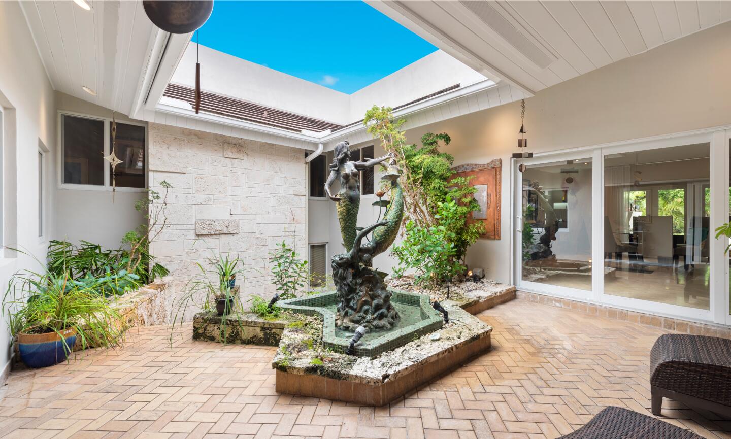 The split-level home wraps around a leafy courtyard anchored by a fountain and mermaid statue.