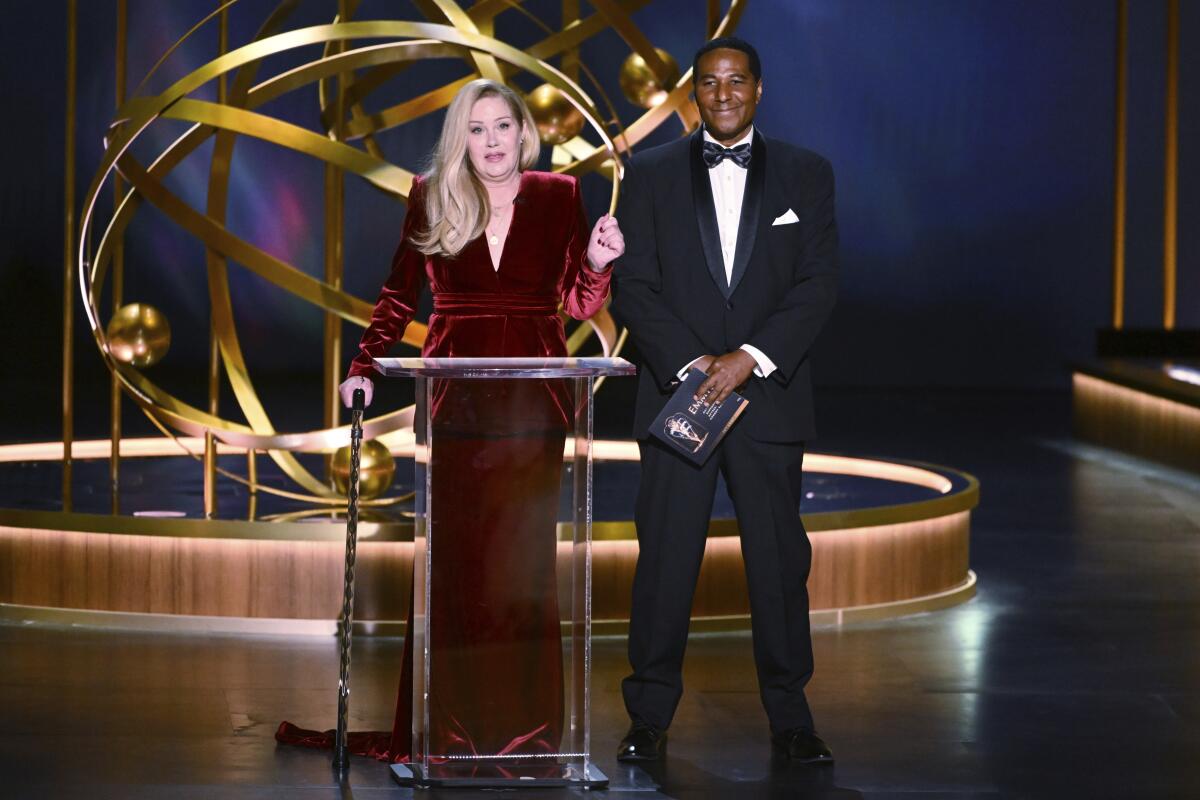 Christina Applegate wears a red velvet gown and stands at a podium. 
