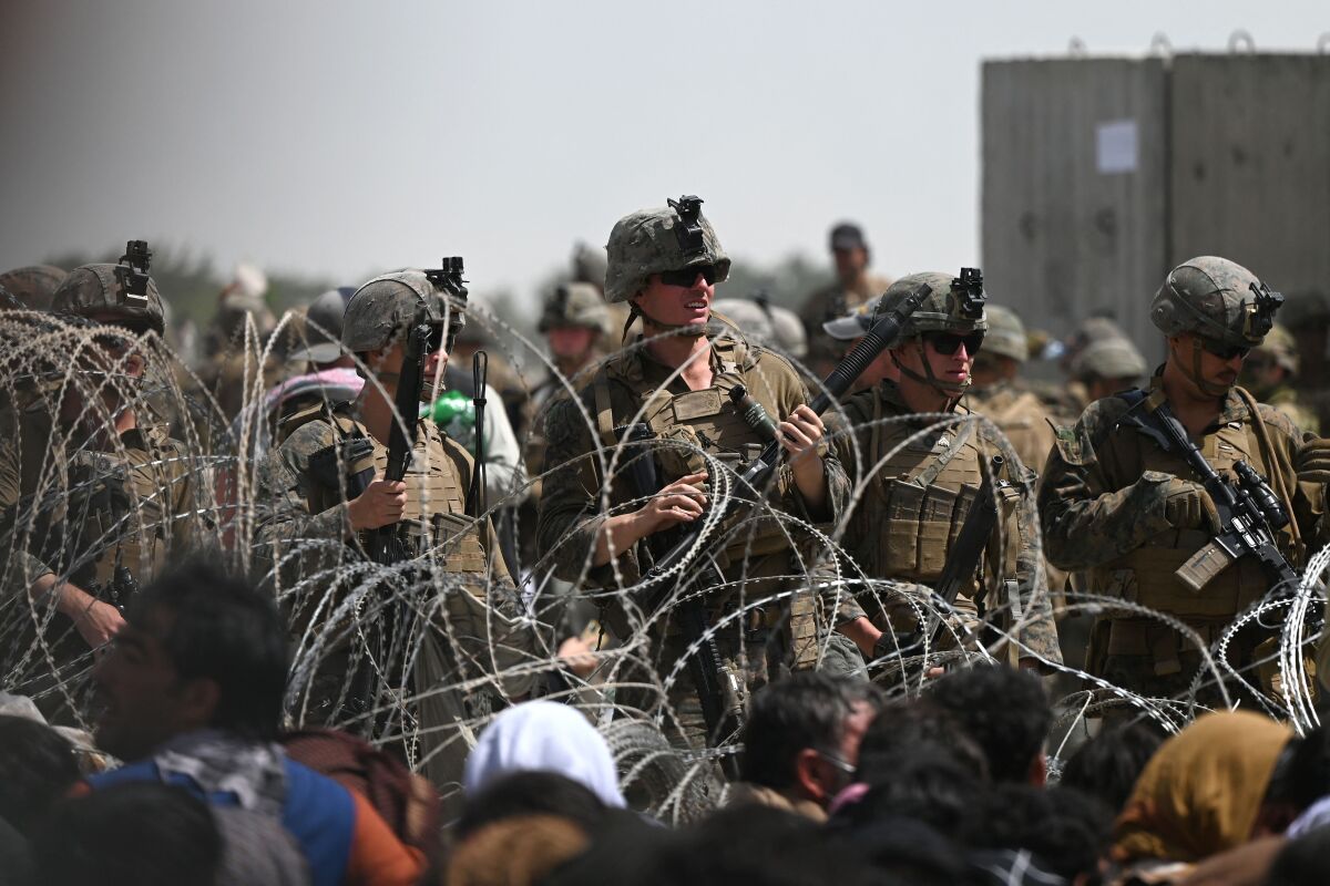 U.S. soldiers stand guard behind a razor wire fence as Afghans wanting to leave the country gather outside Kabul's airport 