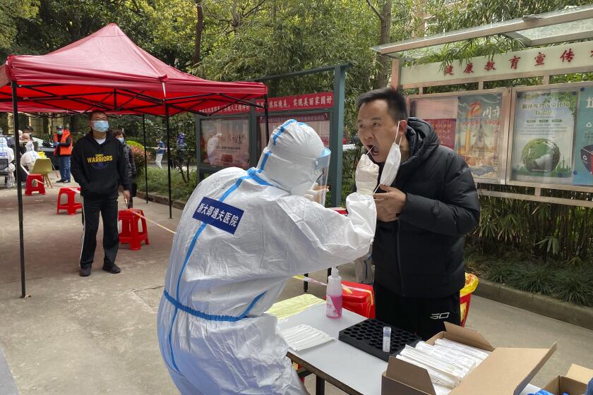 In this photo released by Xinhua News Agency, a medical worker from Zhejiang Province takes a swab sample from a resident for nucleic acid test at a COVID-19 testing site in Pudong District of east China's Shanghai, Monday, March 28, 2022. Chinese authorities sought to reassure companies and jittery investors on Tuesday as a two-phase lockdown of Shanghai's 26 million people entered its second day, casting an unusual quiet over the normally bustling center of finance, manufacturing and trade. (He Zhongming/Xinhua via AP)
