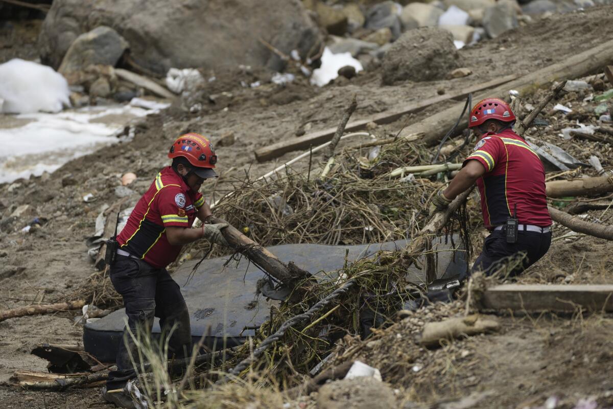 Two people in orange hard hats and red vests clear debris on a slope
