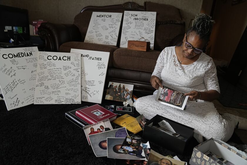 Carolyn Burnett sorts through mementos to select items to commemorate her son Chris Burnett on Sunday, Dec. 5, 2021, in Olathe, Kan. Chris Burnett, an unvaccinated 34-year-old father who coached football at Olathe East High School, died in September as a result of COVID-19 after nearly two weeks on a ventilator. (AP Photo/Charlie Riedel)