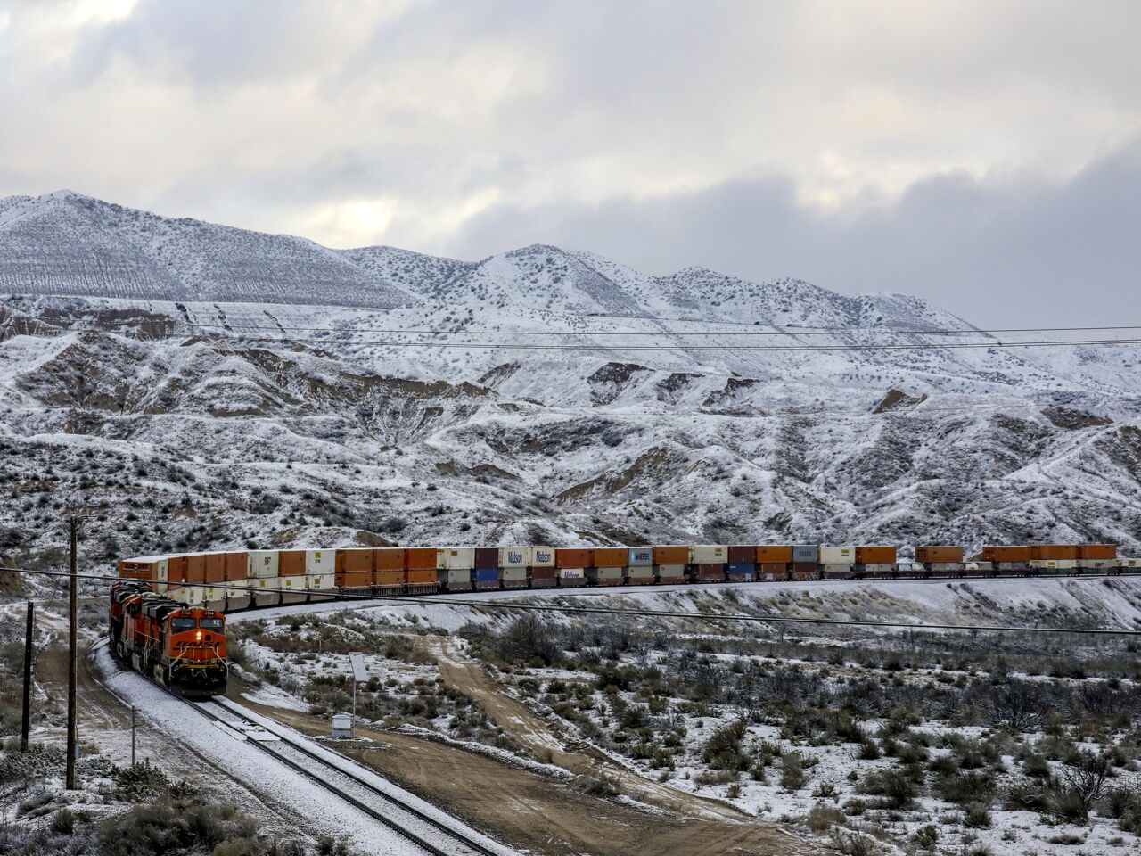 A freight train travels through snowy mountains near the Cajon Pass.