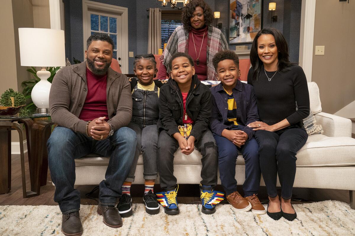 A family poses in a living room. Three children sit on a couch, flanked by two adults. One adult stands behind the couch.