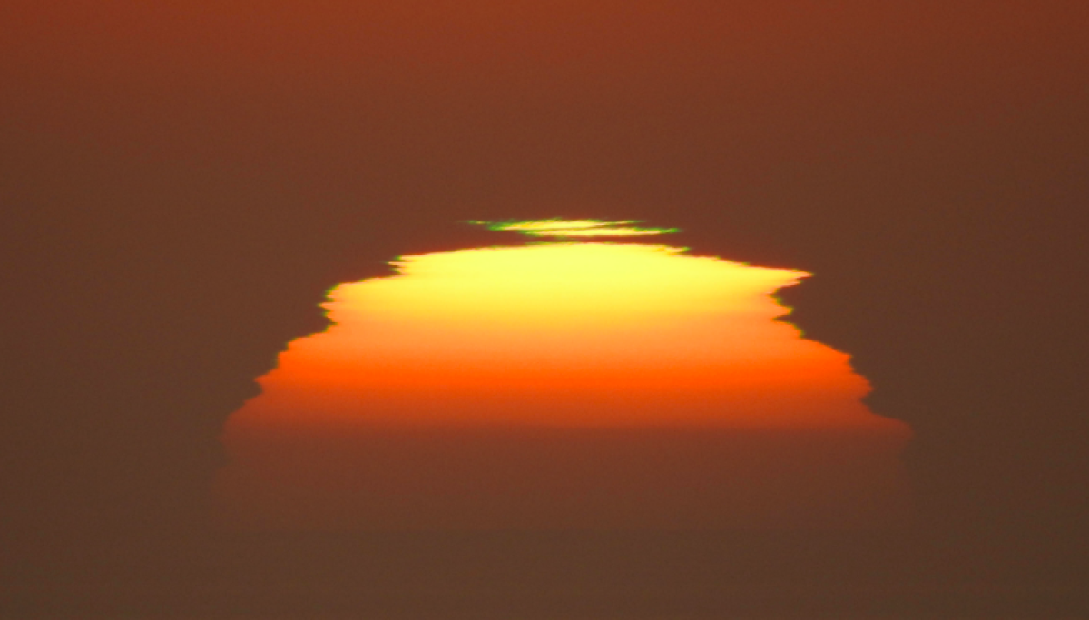 The sun, distorted by smoke and atmosphere, looms in the distance