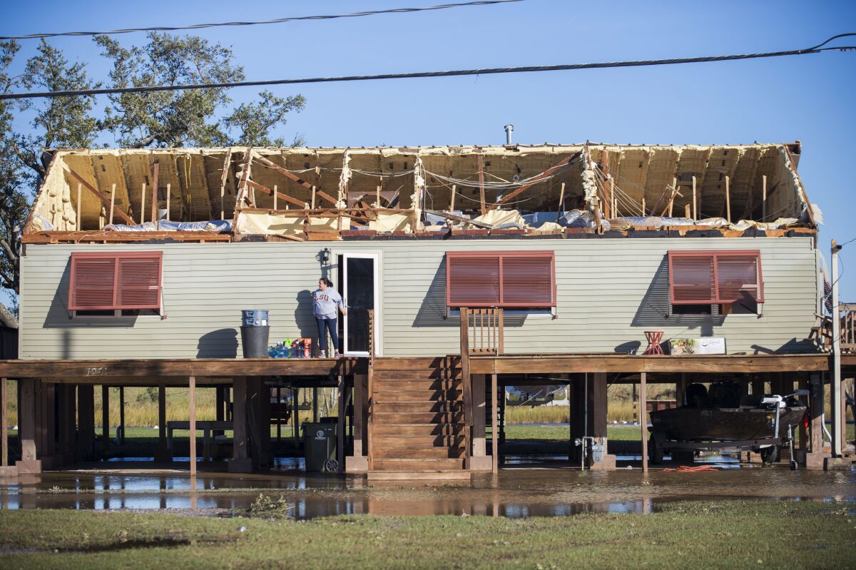 A woman walks out of a house where the roof was torn away during Hurricane Zeta in Chauvin, La.
