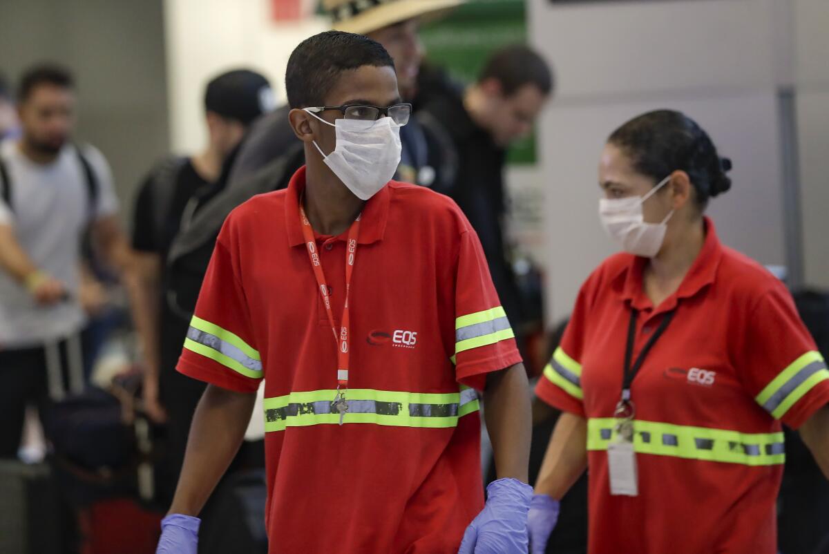 Airport employees wear masks Wednesday at the Sao Paulo International Airport in Brazil.