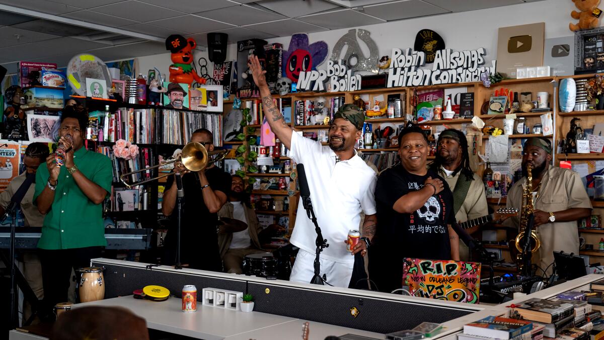 A hip-hop group with a horn section performs in a small space