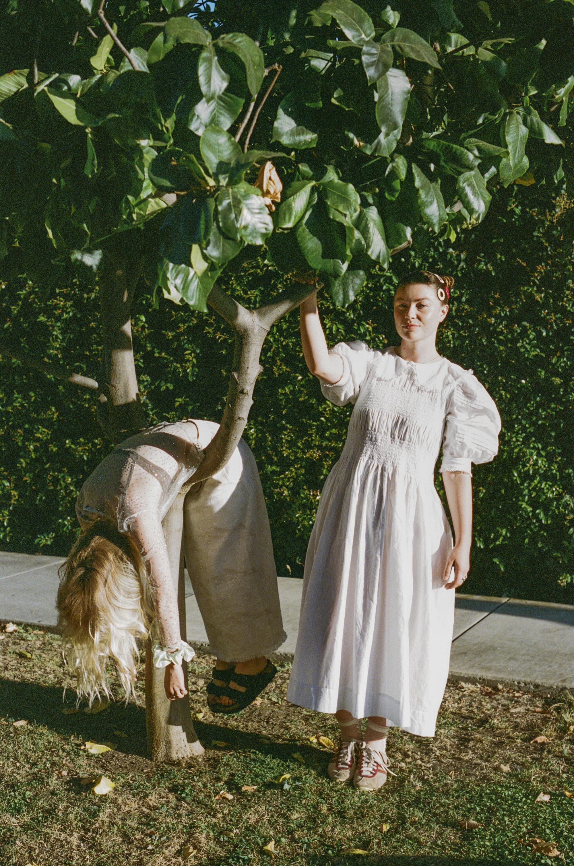 Two women in dresses, the one on the left is draped over a tree branch