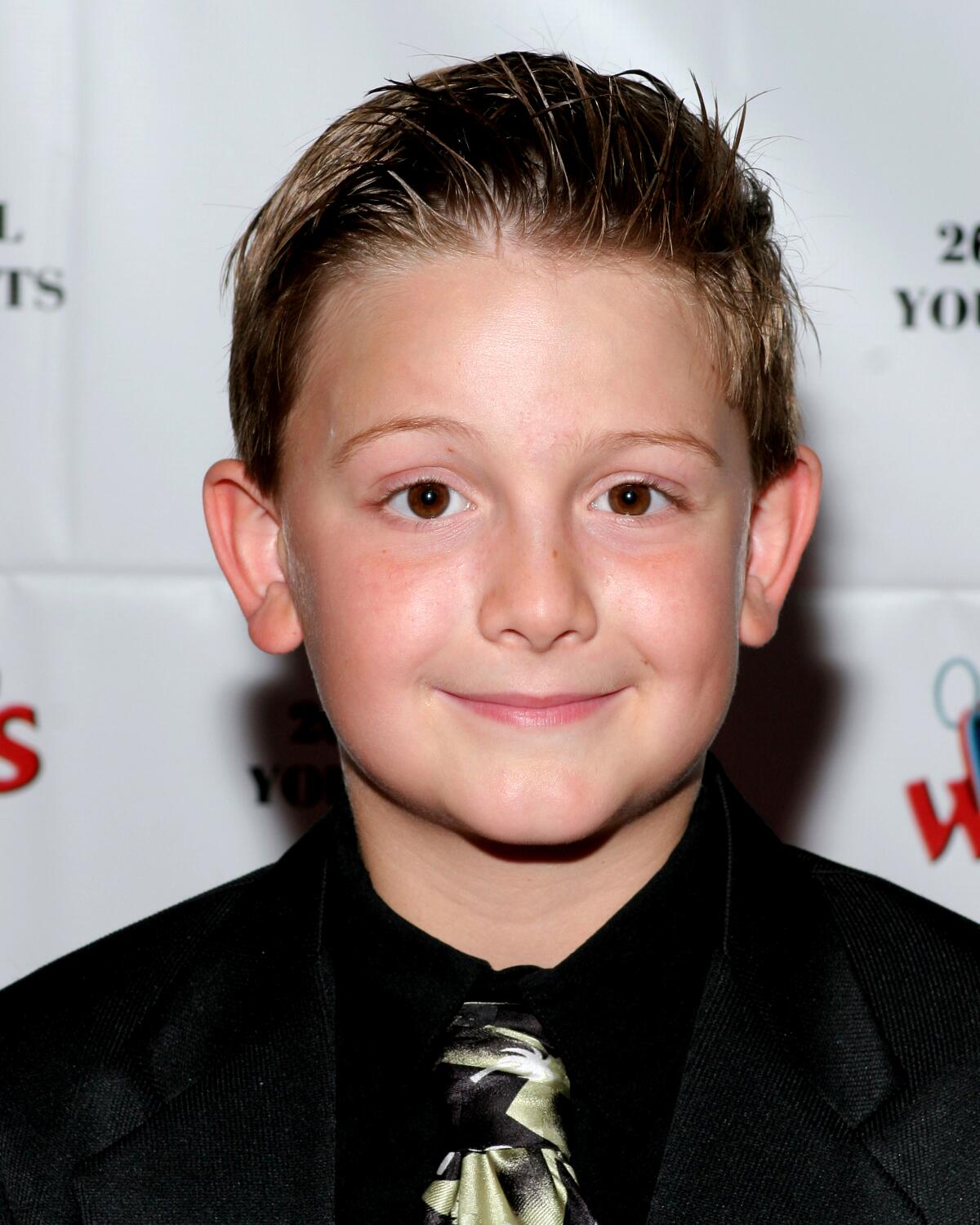 A boy in a black button-up shirt and a tie smiles