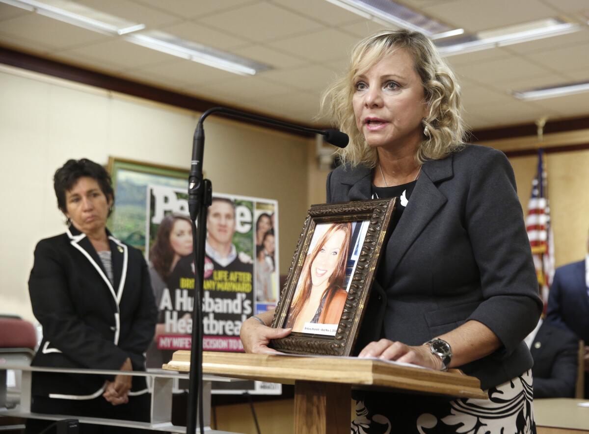 Debbie Ziegler speaks at a lectern holding a photo of her daughter, Brittany Maynard.