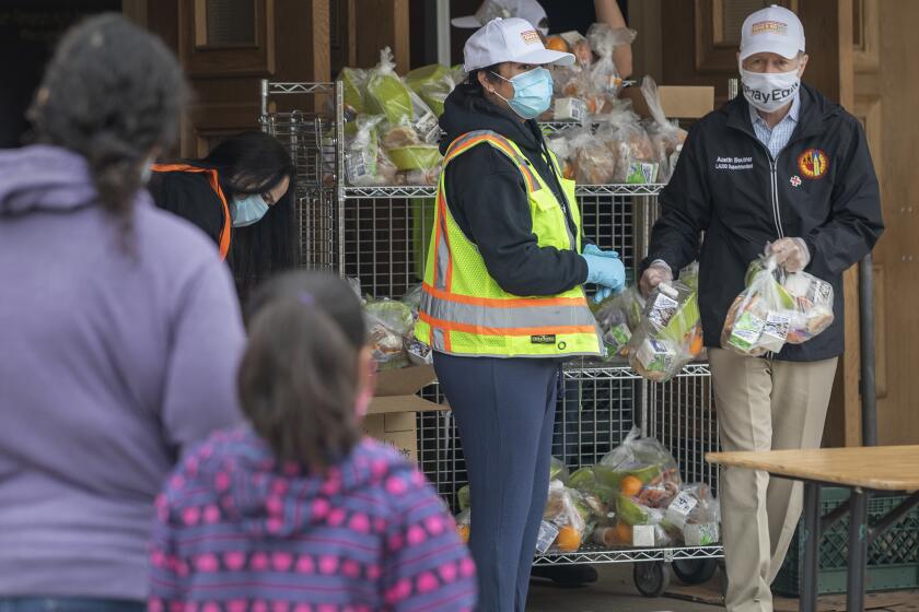 SAN FERNANDO, CA-APRIL 20, 2020: LAUSD Superintendant Austin Beutner, right, wearing a protective mask against the coronavirus, helps distribute food while touring one of the district't Grab & Go food centers at San Fernando Senior High School, where meals were given out to LAUSD students in need. (Mel Melcon/Los Angeles Times)