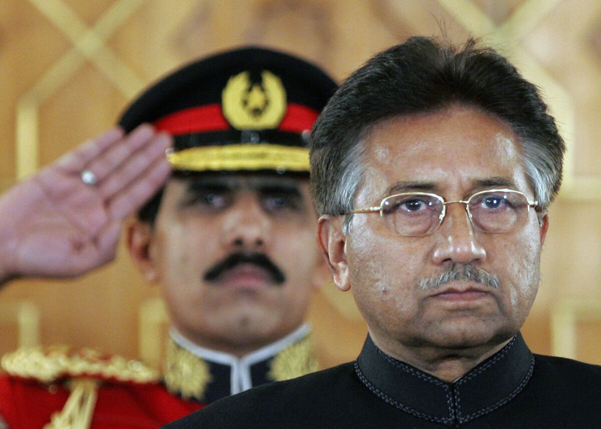 Pervez Musharraf stands in front of a man in uniform saluting.