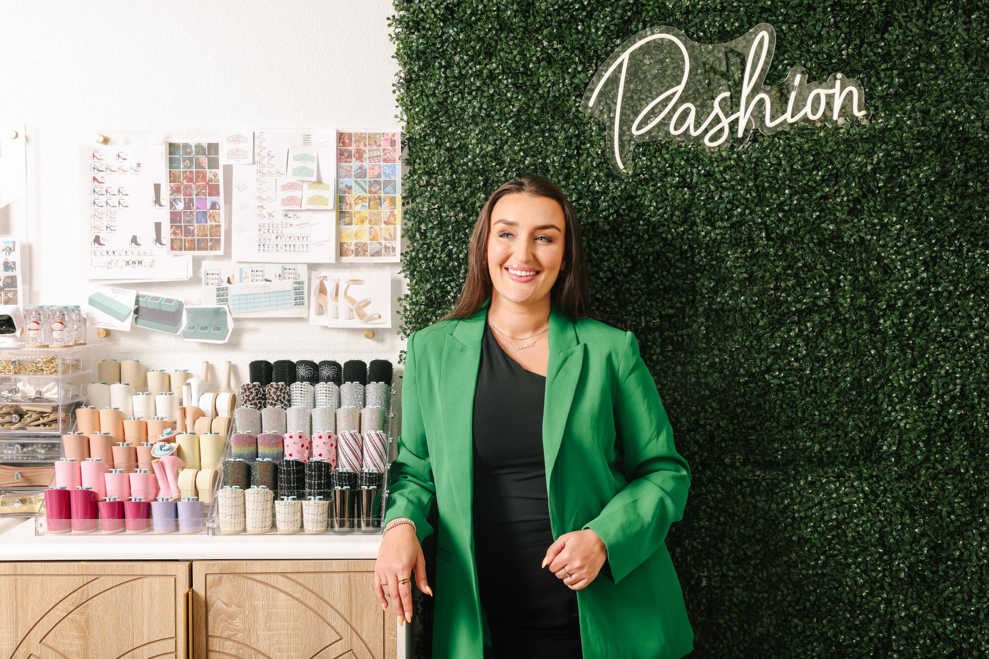 Haley Pavone standing under a "Pashion" sign, one arm on a counter with various materials against a wall showing shoe designs