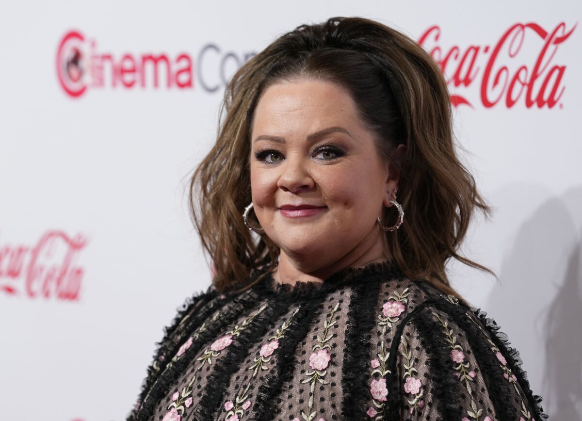 Melissa McCarthy smiles slightly in an outfit with pink flowers and black tulle