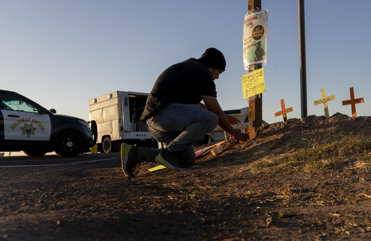 A man kneels to place small wooden crosses in the dirt