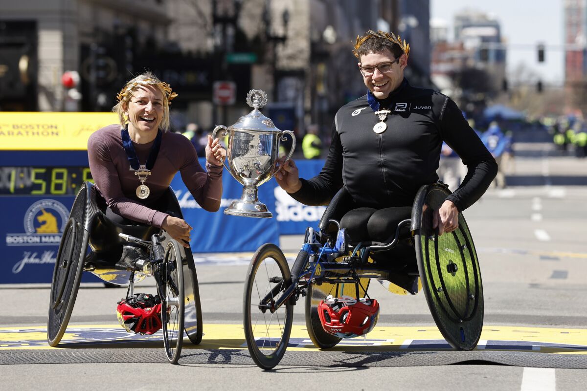 Manuela Schar, of Switzerland, left, and Daniel Romanchuck, of the United States, hold the trophy after winning the men's and women's wheelchair divisions of the 126th Boston Marathon, Monday, April 18, 2022, in Boston. (AP Photo/Winslow Townson)